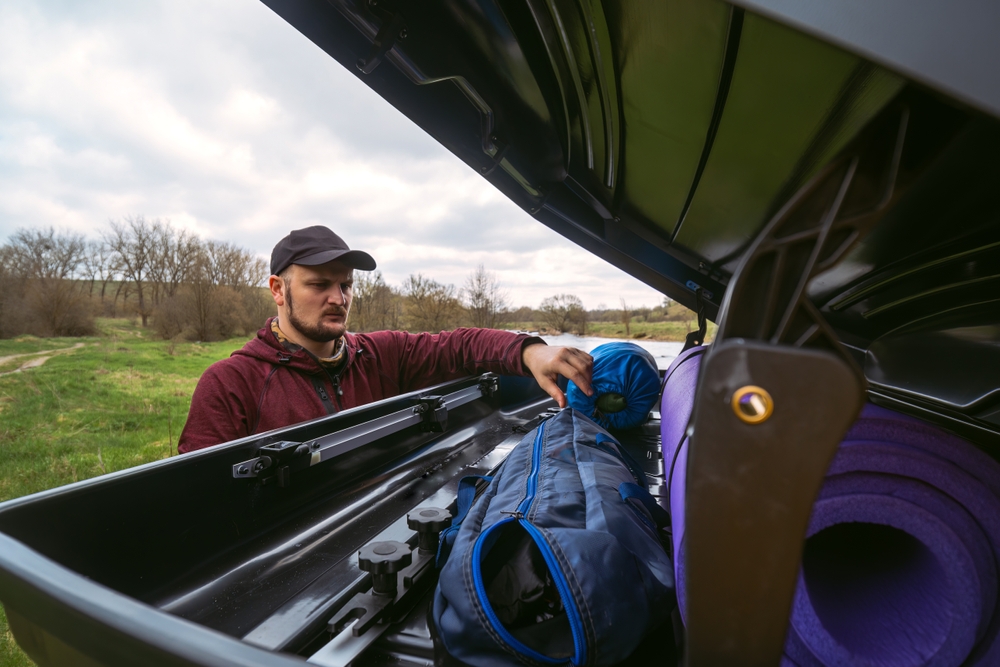 Muž balí turistické vybavenie do strešného boxu auta – efektívne využitie priestoru na cestovanie a outdoorové dobrodružstvá.